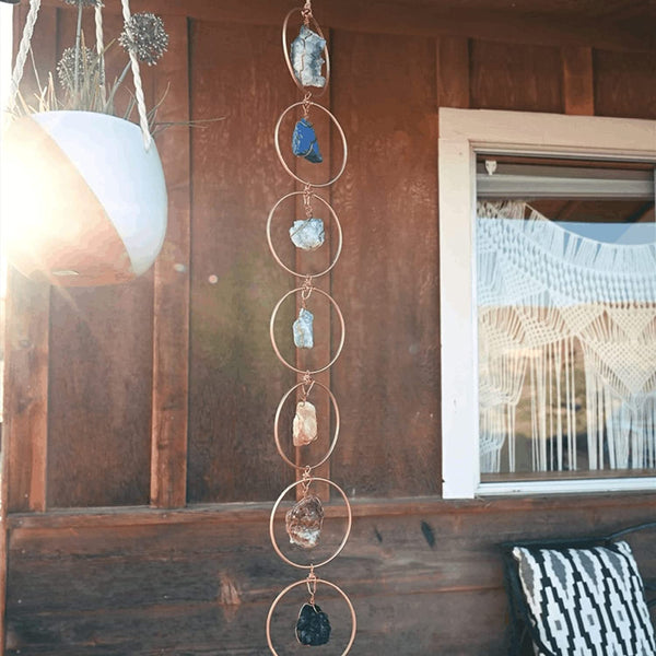 Hangende decoratie met edelstenen in metalen ringen, buiten aan houten muur. Zonlicht reflecteert op de stenen. Boho-stijl, tuin, huisdecoratie.