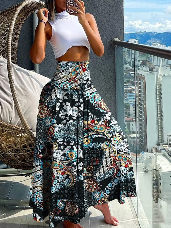 Vrouw in witte crop top en kleurrijke bohemian maxi-rok met bloemenprint op balkon met stadszicht. Zomermode, boho-stijl, trendy outfit.