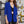 Vrouw in blauwe blazer met opgerolde mouwen, zwarte kanten top en gouden kettingen, tegen een graffiti-muur. Modieuze dameskleding, streetstyle.