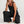 Vrouw in zwarte jumpsuit met wijde pijpen, zittend op de grond. Modieuze dameskleding, casual stijl, comfortabele pasvorm, trendy outfit.