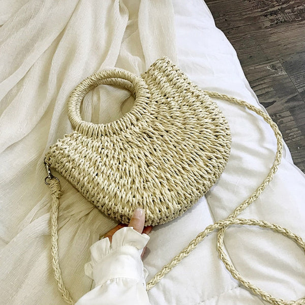Rieten handtas met ronde handvatten en schouderriem op wit beddengoed. Perfecte zomertas, strandtas, boho-stijl accessoire.