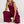 Vrouw in bordeauxrode jumpsuit, zittend op witte achtergrond. Modieuze dameskleding, casual stijl, comfortabele pasvorm, trendy outfit.