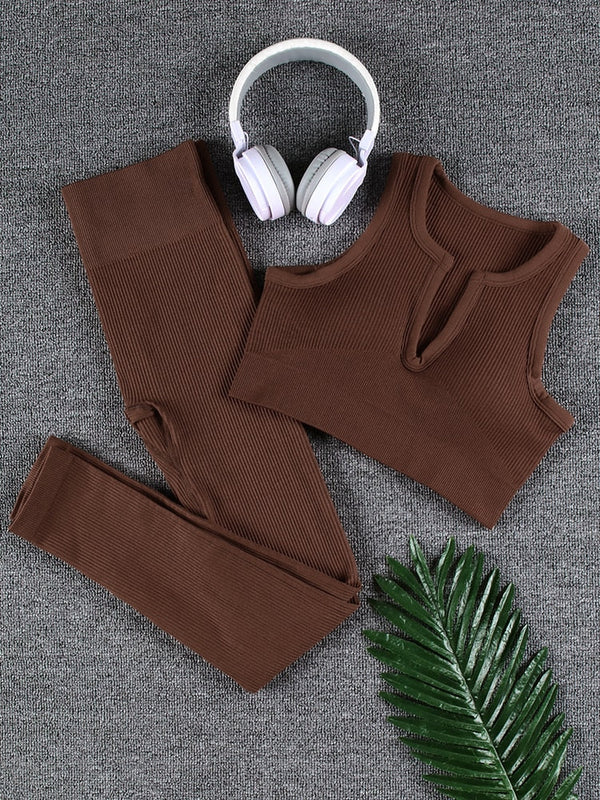 Bruin ribgebreid sportset met crop top en legging, witte koptelefoon en groene palmbladaccessoire op grijze achtergrond. Perfect voor yoga of fitness.
