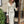 Vrouw in elegante, crèmekleurige geribbelde jurk met ruches en knopen, poseert bij deur. Modieuze dameskleding, herfststijl, stedelijke achtergrond.