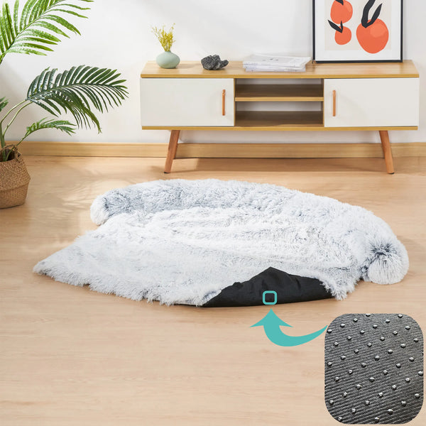 Grijze pluchen hondenmand op houten vloer, met antislip onderkant. Moderne woonkamerinrichting met planten en houten meubel.