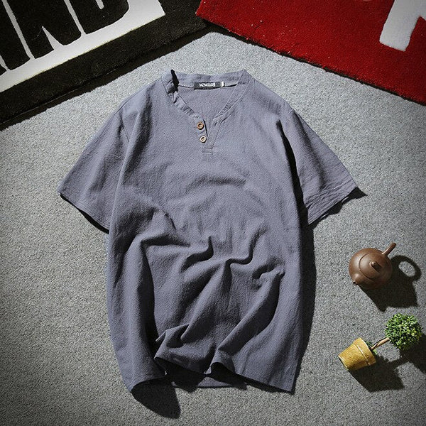 Grijs katoenen T-shirt met knoopsluiting, casual stijl, op grijze vloer met theepot en plant, ideaal voor herenmode en zomerkleding.