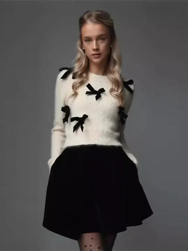Jonge vrouw in stijlvolle outfit met witte trui met zwarte strikjes en zwarte rok, modefotografie, herfst-winter kledingstijl.