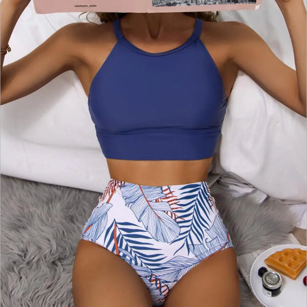 Vrouw in blauwe crop top en tropische hoge taille bikini, liggend op bed met boek. Trendy damesmode, zomeroutfit, strandkleding.