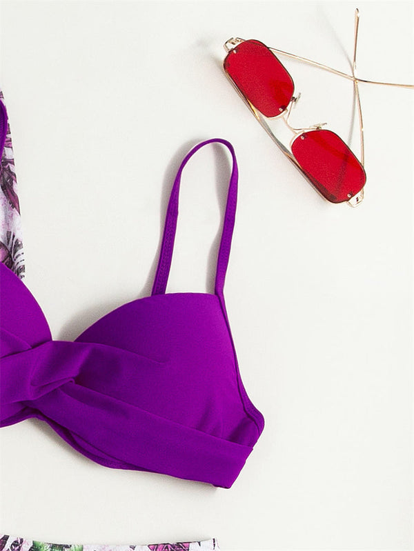 Paarse bikini top met gedraaide voorkant en dunne bandjes, naast rode zonnebril op witte achtergrond. Zomermode, strandkleding, accessoires.