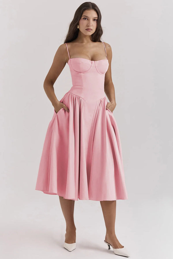Vrouw in roze midi-jurk met spaghettibandjes en wijde rok, poseert tegen een neutrale achtergrond. Perfect voor zomer- of cocktailfeesten.