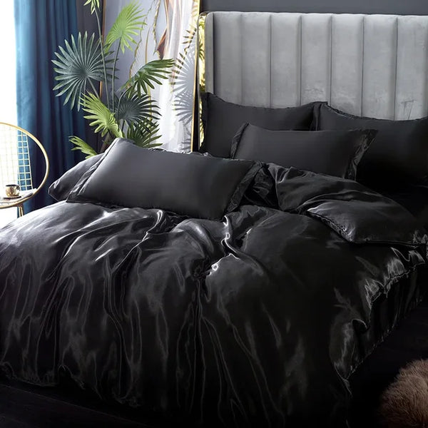 Luxe zwart satijnen dekbedovertrek op kingsize bed met grijze hoofdbord, omgeven door groene planten en gouden bijzettafel. Elegante slaapkamerinrichting.