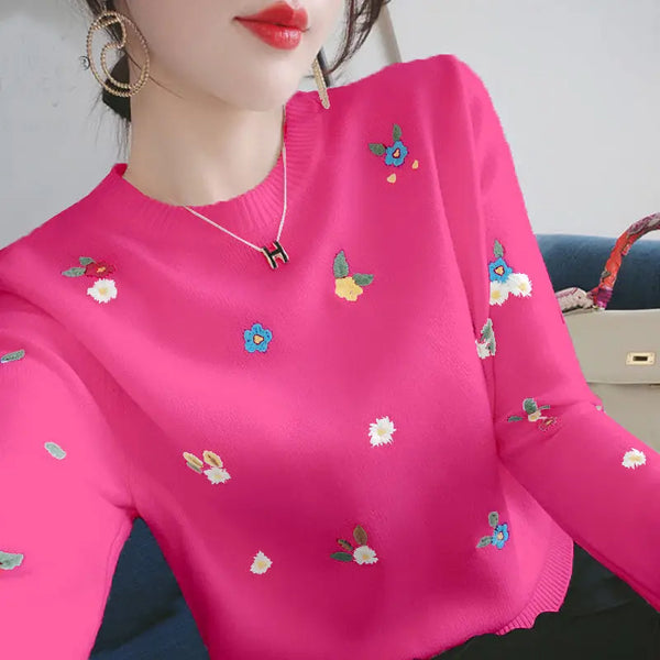 Vrouw draagt felroze trui met kleurrijke bloemenborduursels, gouden oorbellen en een H-hanger ketting. Modieuze dameskleding, trendy stijl.