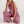 Vrouw in roze linnen jumpsuit met wijde pijpen, zittend op witte achtergrond. Modieuze dameskleding, casual zomeroutfit, comfortabele stijl.
