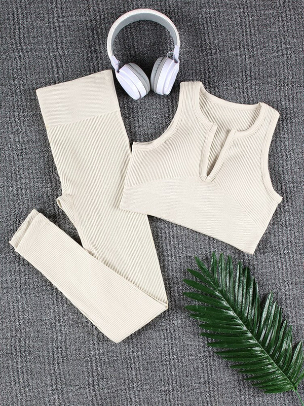 Crèmekleurige ribgebreide sportset met top en legging, naast witte koptelefoon en groene palmbladaccessoire op grijze achtergrond.