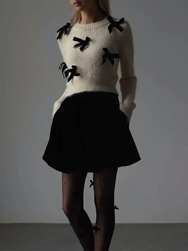 Vrouw in stijlvolle outfit met witte trui met zwarte strikjes, zwarte rok en panty met strikdetails. Modieuze dameskleding, herfstmode.