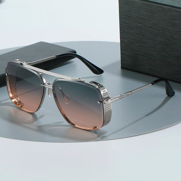 Zilveren aviator zonnebril met bruine gradient glazen op een grijze achtergrond, naast een zwarte doos. Stijlvol en modern ontwerp voor herenmode.