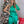 Vrouw in groene satijnen jurk voor versierde kerstboom, glimlachend. Kerstdecoratie, feestelijke sfeer, moderne kerstmode.