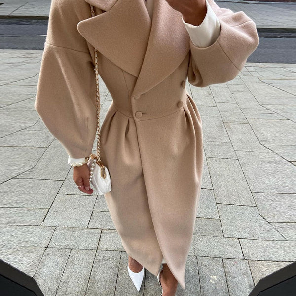 Vrouw in elegante beige wollen jas met dubbele rij knopen, witte handtas en hakken. Modieuze herfstoutfit, stedelijke achtergrond.