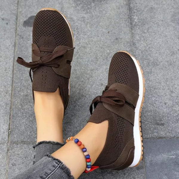 Bruine dames sneakers met veters, ademend mesh, comfortabele zool, gedragen met grijze jeans en kleurrijke enkelband, op grijze tegelvloer.