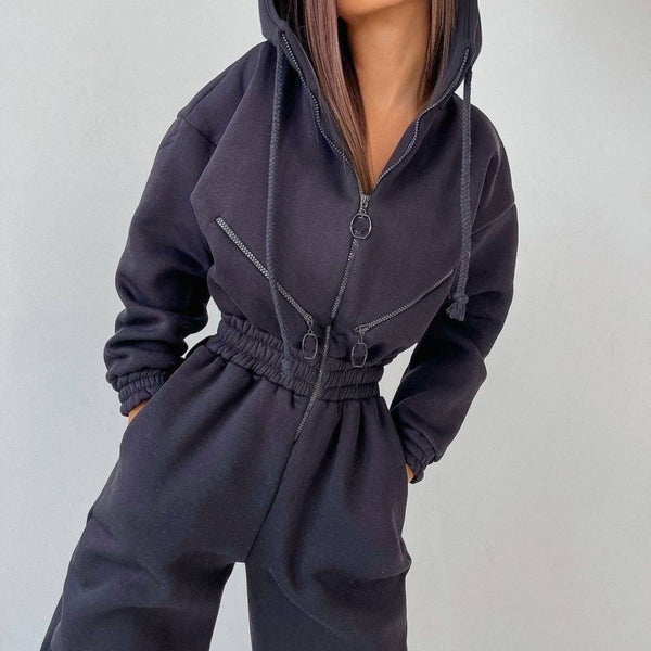 Vrouw in zwarte hoodie jumpsuit met capuchon, ritssluitingen en elastische taille. Modieuze streetwear outfit voor dames.