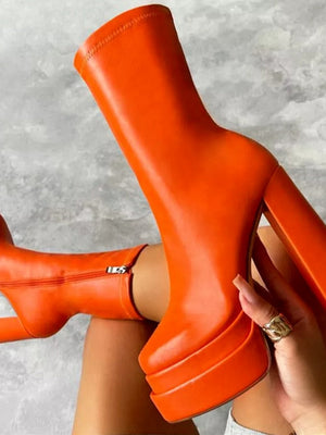 Oranje platformlaarzen met hoge hakken, trendy design, gedragen door een persoon. Perfect voor modieuze herfst- en winteroutfits.