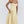 Vrouw in elegante gele midi-jurk met spaghettibandjes, strapless ontwerp en geplooide rok. Perfect voor zomermode en feestelijke gelegenheden.