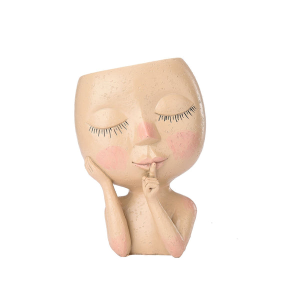 Decoratieve plantenpot in de vorm van een gezicht met gesloten ogen en vinger op de lippen, beige kleur, geschikt voor interieurdecoratie.