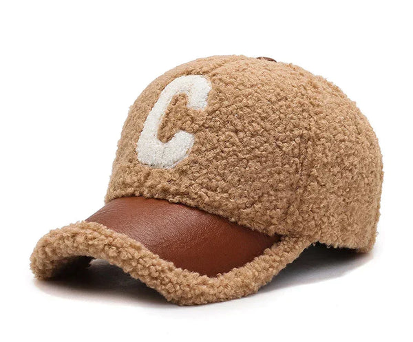 Bruine teddy cap met witte letter "C" en leren klep. Modieuze winterpet, warme textuur, trendy accessoire voor koude seizoenen.