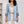 Vrouw in lichtblauwe blazer met opgerolde mouwen, witte kanten top en witte broek. Modieuze dameskleding, casual chic stijl.