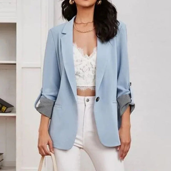 Vrouw in lichtblauwe blazer met opgerolde mouwen, witte kanten top en witte broek. Modieuze dameskleding, casual chic stijl.