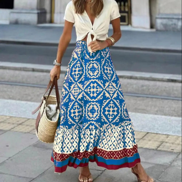 Vrouw in bohemian maxi rok met blauw-wit patroon en knoopblouse, draagt rieten tas. Zomerse mode, straatstijl, casual chique outfit.