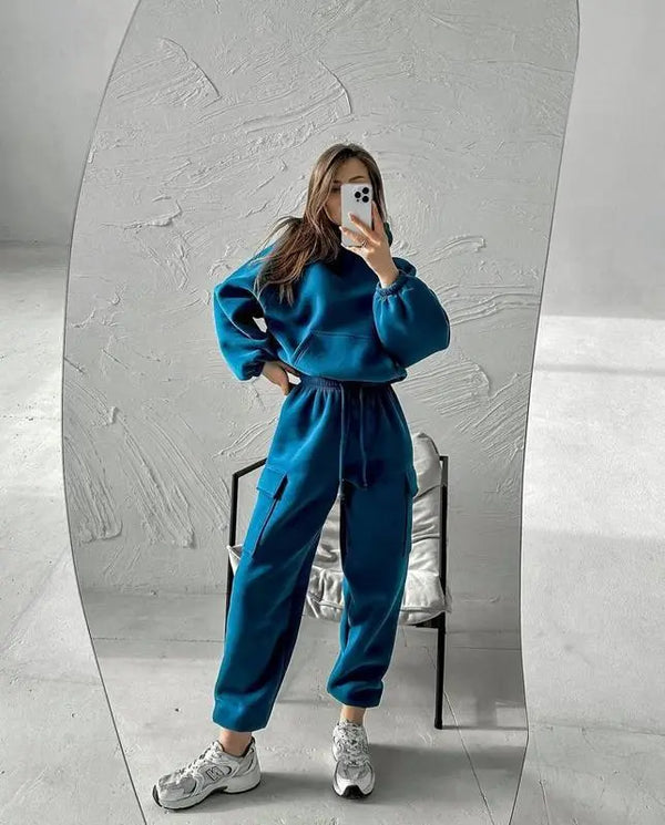 Vrouw in blauwe joggingpak en witte sneakers maakt selfie in spiegel. Moderne casual mode, comfortabele loungewear, minimalistisch interieur.