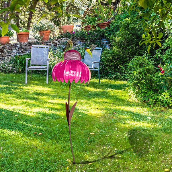 Roze metalen bloemtuinlamp in zonnige tuin met groene grasmat, omgeven door planten en twee stoelen. Decoratieve buitenverlichting, tuinaccessoires.