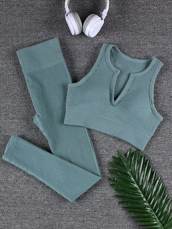 Groene naadloze sportset met legging en crop top op grijze achtergrond, naast witte koptelefoon en groene palmblad. Sportkleding voor dames.
