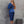 Vrouw in elegante blauwe satijnen jurk met asymmetrische schouder, staand tegen een betonnen muur. Stijlvolle mode, avondkleding, chique uitstraling.