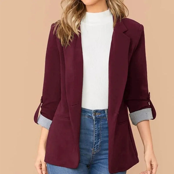 Vrouw in bordeaux blazer met opgerolde mouwen, witte coltrui en blauwe jeans. Modieuze dameskleding, casual chic stijl.