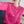 Vrouw in felroze trui met kleurrijke bloemenborduursels, zittend op een blauwe bank. Trendy damesmode, casual outfit, herfstkleding.