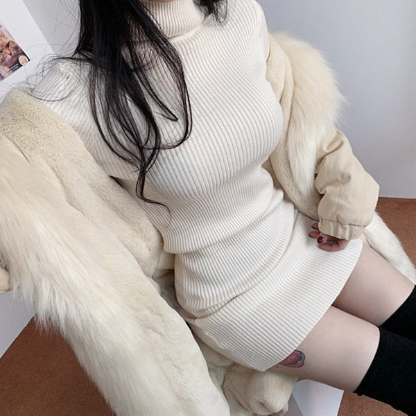 Vrouw in crèmekleurige geribbelde coltrui-jurk met witte bontjas, zittend op een stoel. Modieuze winterkleding, trendy damesmode.