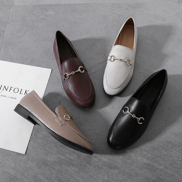 Vier stijlvolle loafers in verschillende kleuren op een grijze achtergrond, met metalen details. Perfect voor modieuze dames. Luxe schoenen, trendy design.