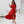Vrouw in elegante rode off-shoulder jurk met ruches, staand in moderne witte woonkamer. Trendy zomeroutfit, modieuze dameskleding.