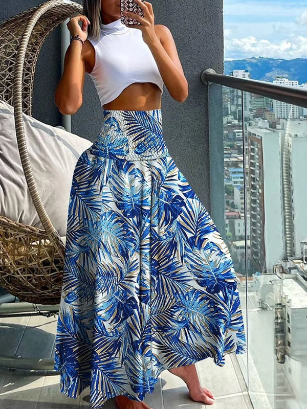 Vrouw in witte crop top en blauwe tropische maxi-rok op balkon met stad en bergen op achtergrond. Zomermode, stedelijk uitzicht, trendy outfit.
