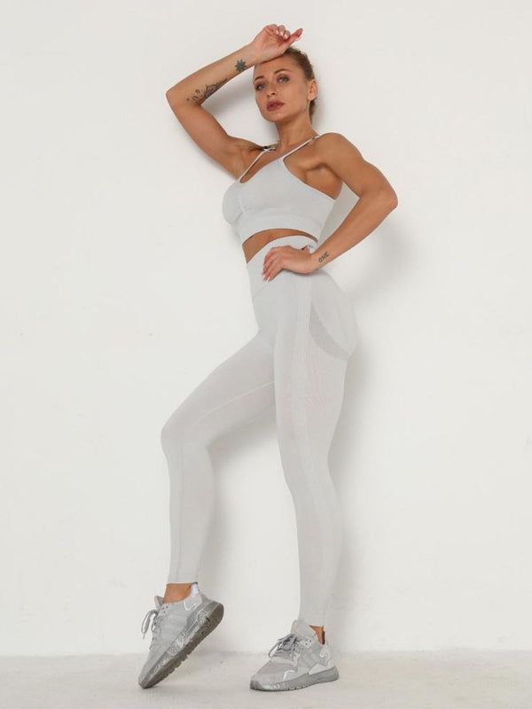 Vrouw in grijze sportkleding poseert tegen witte achtergrond, draagt naadloze legging en sportbeha, met grijze sneakers. Fitnessmode, actieve levensstijl.