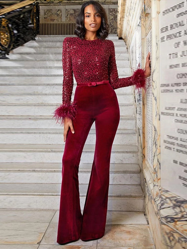 Vrouw in elegante rode jumpsuit met pailletten en veren, poseert op marmeren trap. Modieuze avondkleding, glamour, stijlvolle outfit.