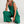 Vrouw in groene jumpsuit met wijde pijpen, zittend op witte achtergrond. Modieuze dameskleding, casual stijl, comfortabele pasvorm.