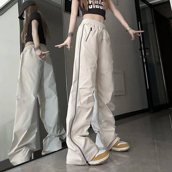 Vrouw in trendy beige wijde broek met ritsen, zwarte crop top en gele sneakers poseert voor spiegel. Streetwear mode, casual outfit.