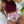 Vrouw in bordeauxrode crop top en tropische hoge taille bikini met bladerenprint, liggend op wit beddengoed naast ananas en hoed.