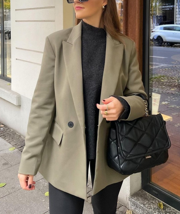 Vrouw in stijlvolle beige blazer met zwarte trui en gewatteerde zwarte handtas, wandelend op straat. Mode, herfstkleding, damesmode.