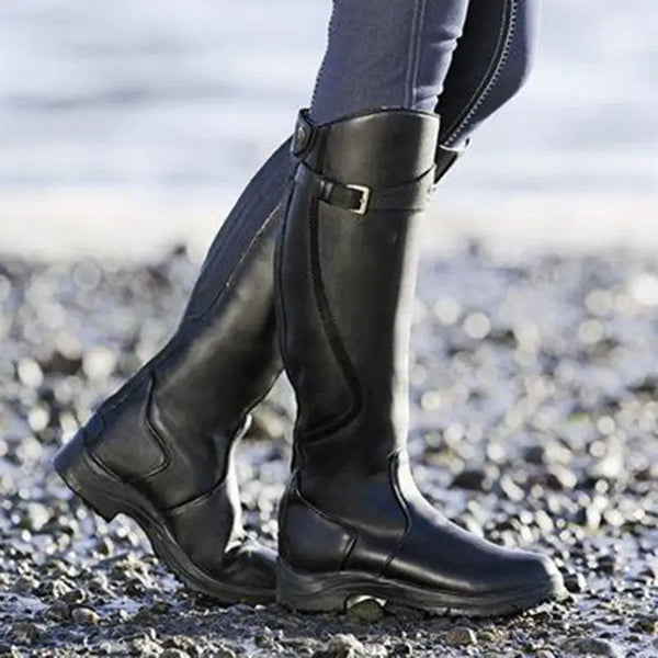 Zwarte leren rijlaarzen op kiezelstrand, waterdicht en duurzaam, ideaal voor paardrijden en outdoor activiteiten. Comfortabele pasvorm.
