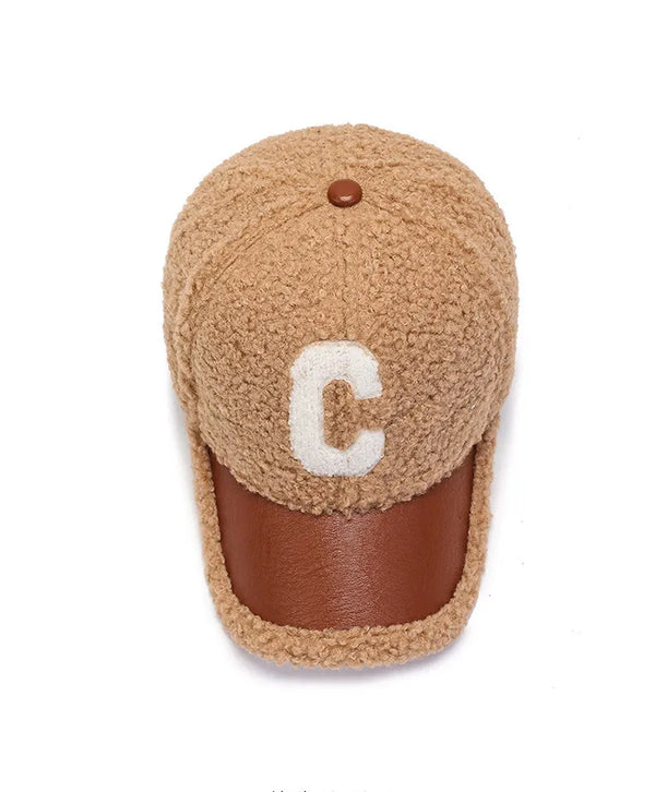 Bruine sherpa pet met leren klep en witte letter "C". Stijlvolle winteraccessoire, unisex design, perfect voor casual en trendy outfits.