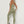 Vrouw in groene sportlegging en sportbeha, poseert tegen witte achtergrond. Fitnesskleding, sportoutfit, actieve levensstijl.